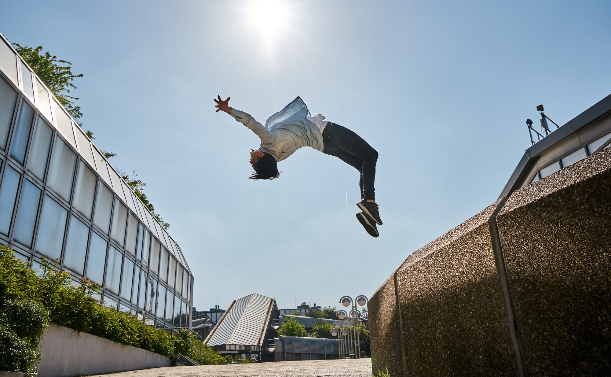 Ein athletischer Mensch macht in der Sonne einen Rückwärtssalto, im Hintergrund sind moderne Gebäude. Er symbolisiert Kraft und Ausdauer durch NADH - Coenzym1.