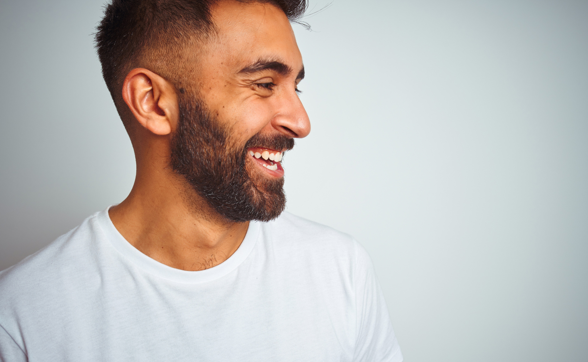 Ein Mann mit Bart, der lachend zur Seite schaut und einen weißen Pullover trägt. Ein Symbolfoto für mentale Gesundheit mit ausgewählten Mikronährstoffen.
