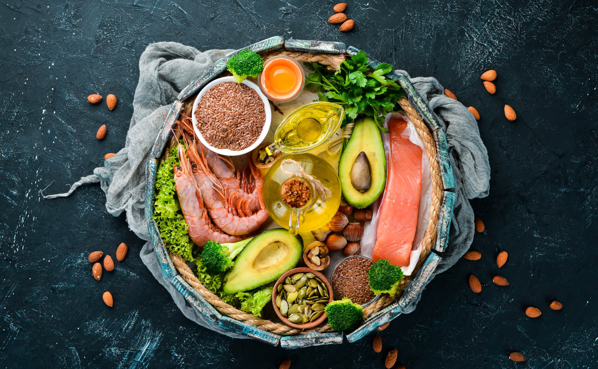 Eine rustikale Platte, gefüllt mit Omega-3-reichen Lebensmitteln wie Lachs, Garnelen, Avocado, Leinsamen, Nüssen und Ölen auf dunklen Hintergrund.