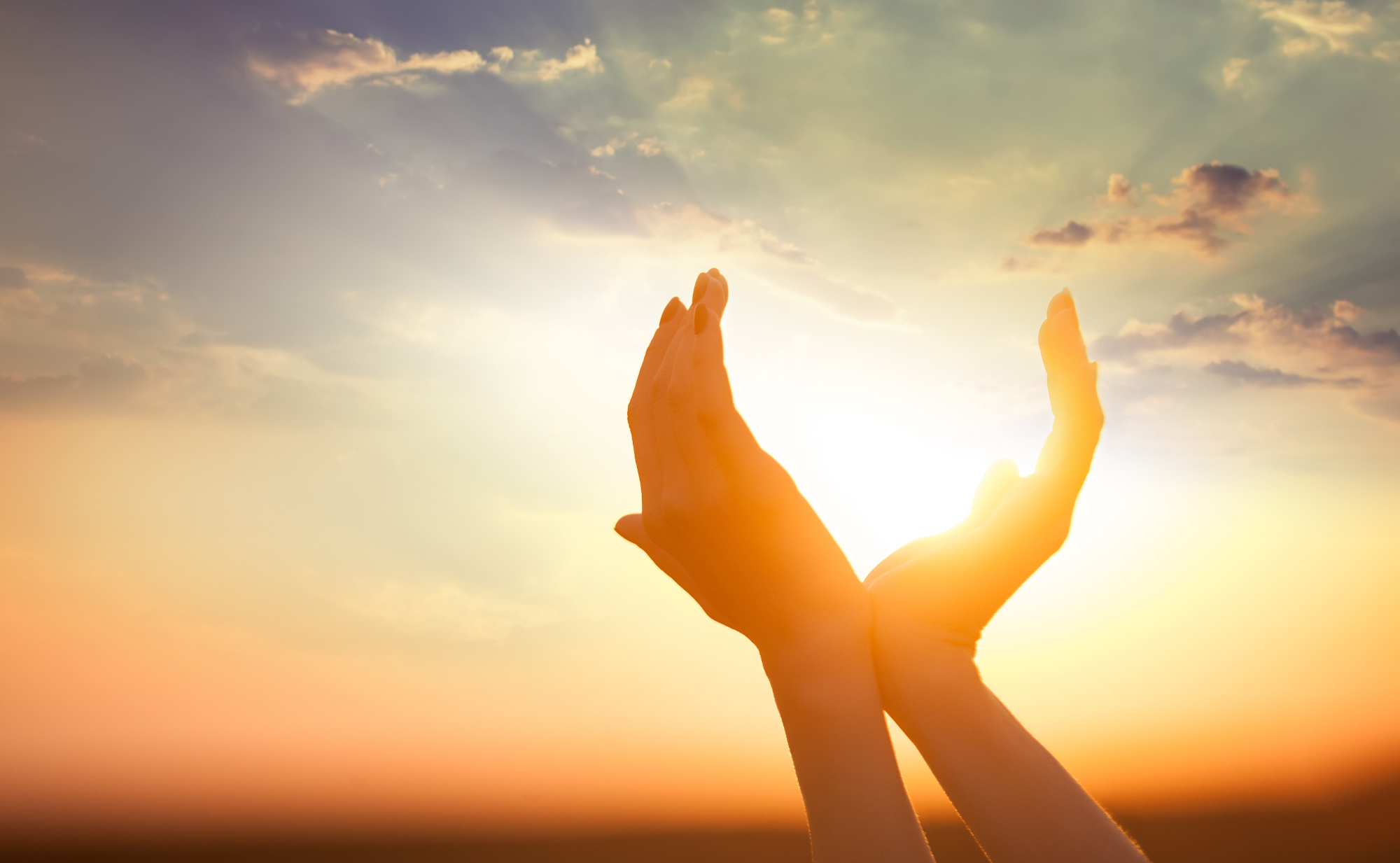 Zwei Hände rahmen die untergehende Sonne ein, mit einem farbenprächtigen Himmel im Hintergrund. Das Bild steht symbolisch für die Kraft der Sonne und natürlichen Sonnenschutz.