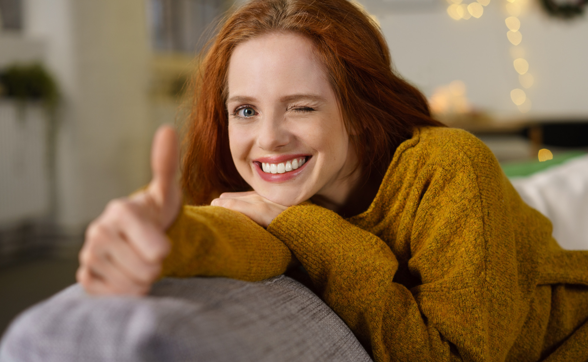 Eine Frau mit roten Haaren zwinkert und zeigt den Daumen nach oben, während sie auf einem Sofa liegt. Ein Symbolfoto für Wohlbefinden mit dem richtigen Gewicht.